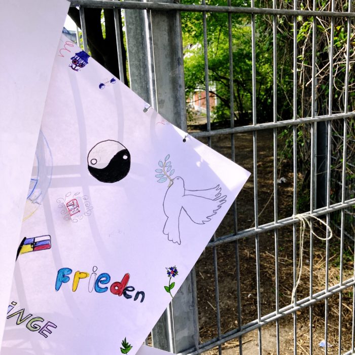 Eine Kinderzeichnung einer Friedenstaube hängt an einem Schulzaun
