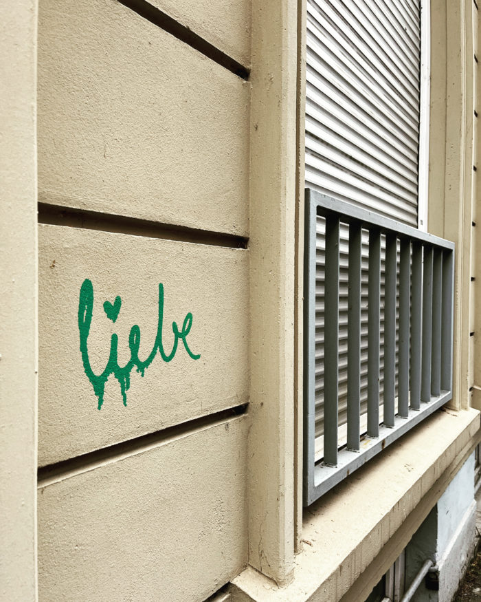 Ein Schriftzug "liebe" in grüner Farbe an einer Hauswand