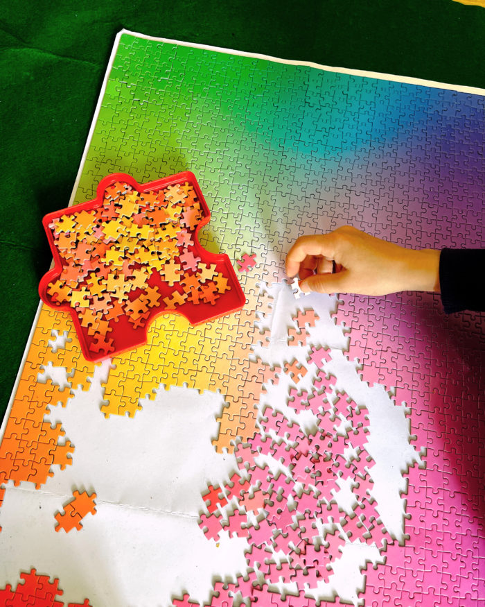 Eine Hand über einem 1000er Puzzle, das nureinen Farbverlauf darstellt, kein gegenständliches Motiv.