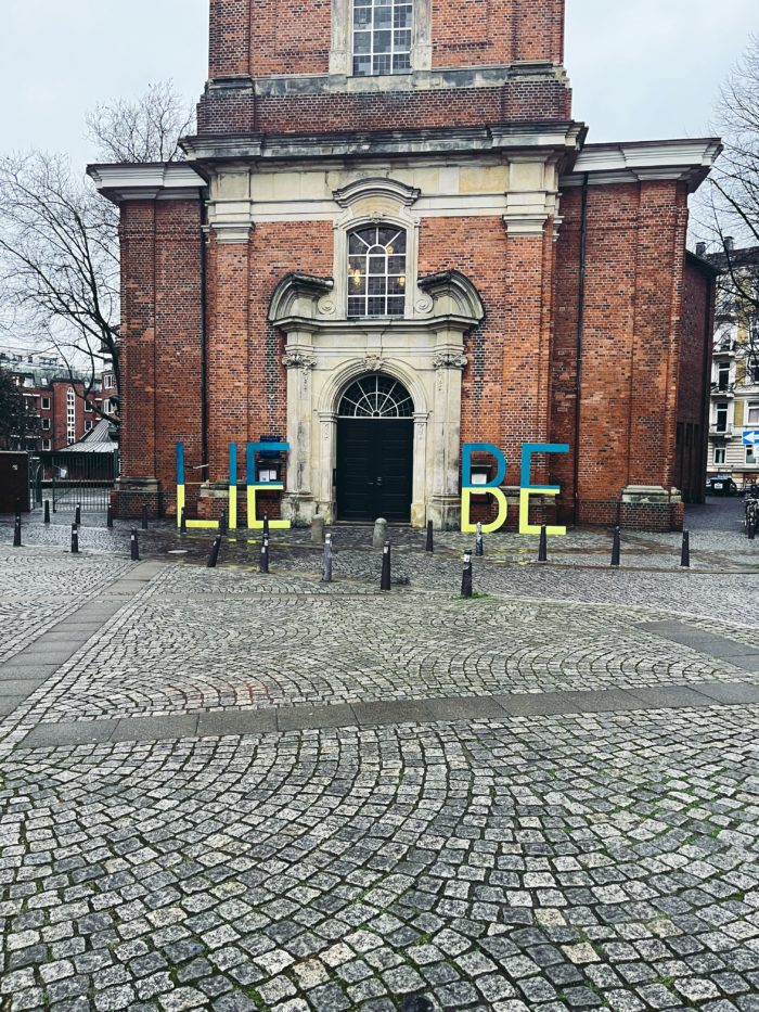 Das Portal einer Kirche, große blaugelbe Holzbuchstaben formen davor das Wort LIEBE.