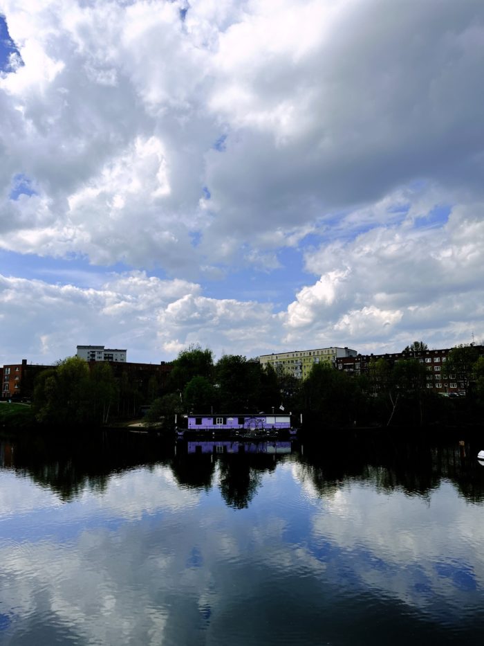 Ein lilafarbenes Hausboot auf der Bille unter bewölktem Himmel