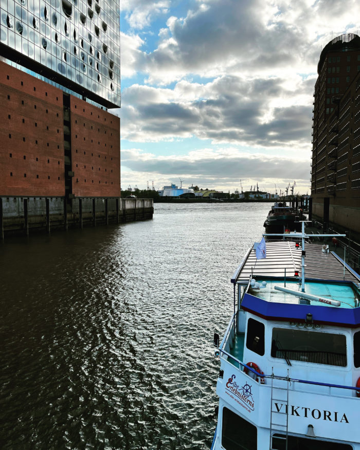 Seitlicher Blick auf den unteren Teil der Elbphilharmonie, im Vordergrund ein Schiff namens "Victoria"