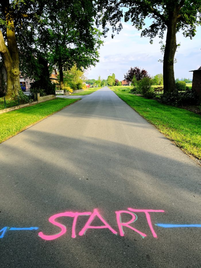 Eine aufgemalte Startlinie auf einer ländlichen Straße, man sieht das Wort "Start" auf dem Asphalt