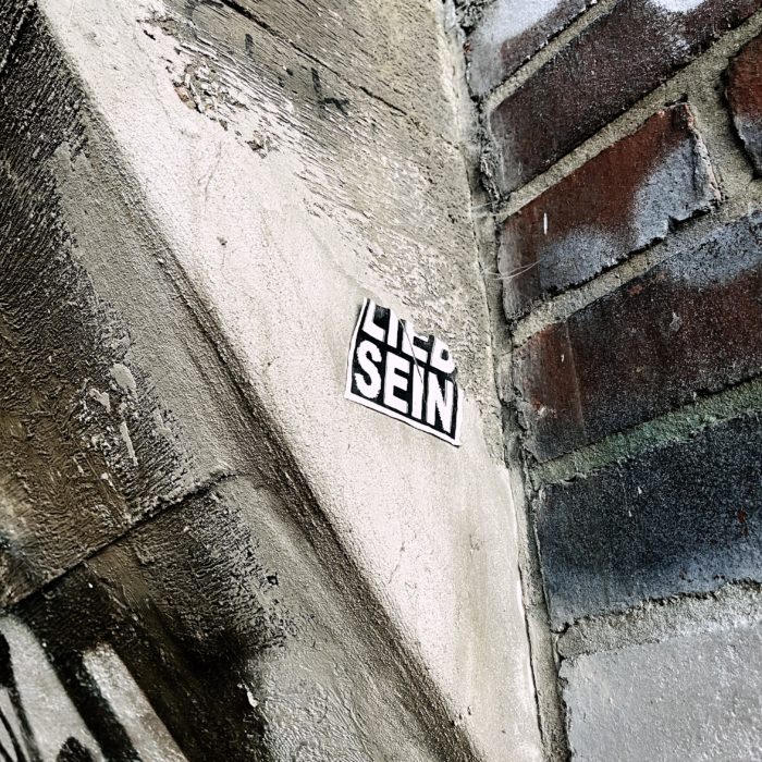 Ein halb abgerissener Aufkleber mit der Aufschrift "LIEB SEIN" unter einer Brücke, gerade noch zu lesen
