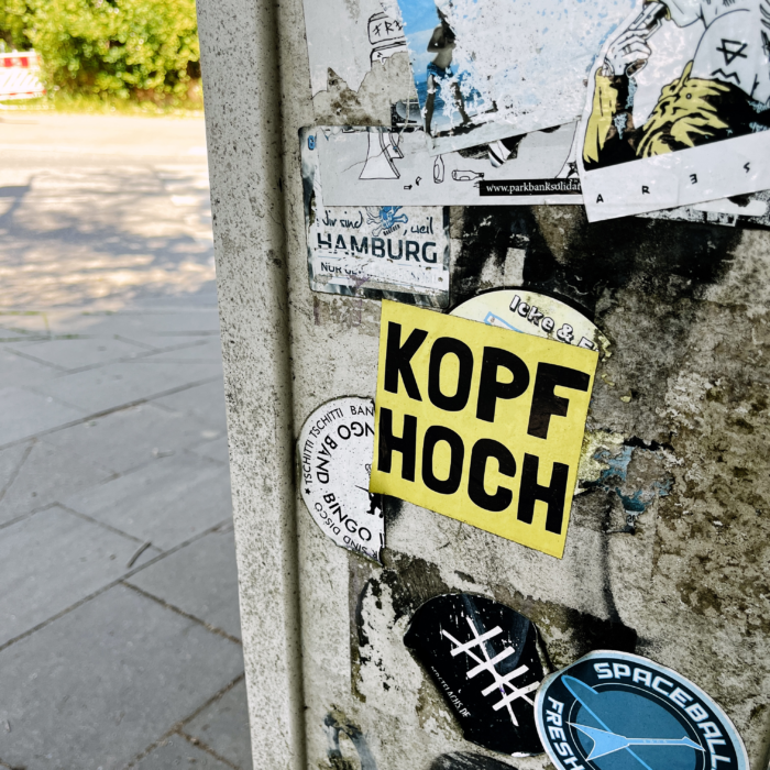 Ein Sticker auf einem Stromkasten mit dem Text "Kopf hoch"