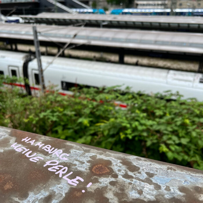 Ein Schriftzug auf dem Geländer der Ernst-Merck-Brücke am Hauptbahnhof: Hamburg meine Perle. Im Hintergrund Züge.
