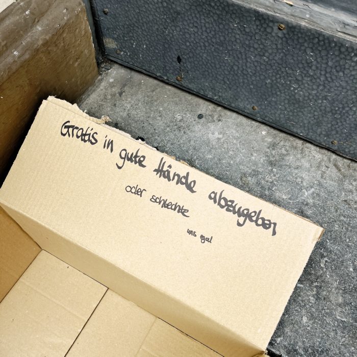 Ein Pappkarton auf einer Treppe, auf dem Deckel steht "Gratis in gute Hände abzugeben - oder in schlechte, ist uns egal"