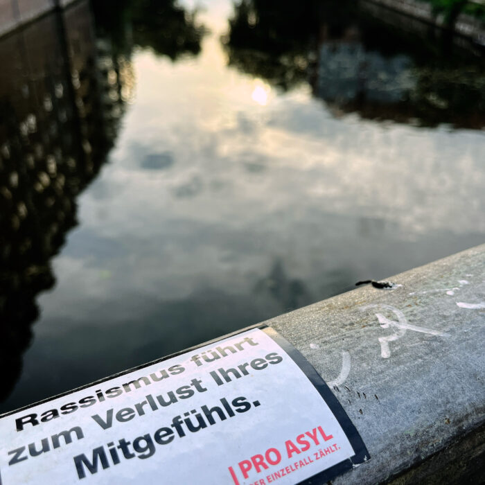 Ein Aufkleber von Pro Asyl an einem Brückengeländer, Text: "Rassismus führt zum Verlust Ihres Mitgefühls"