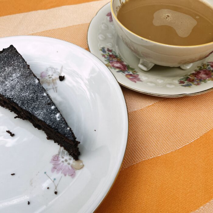 Ein Stück Schokoladenkuchen auf einem altmodischen Teller, daneben eine Tasse mit Füßchen