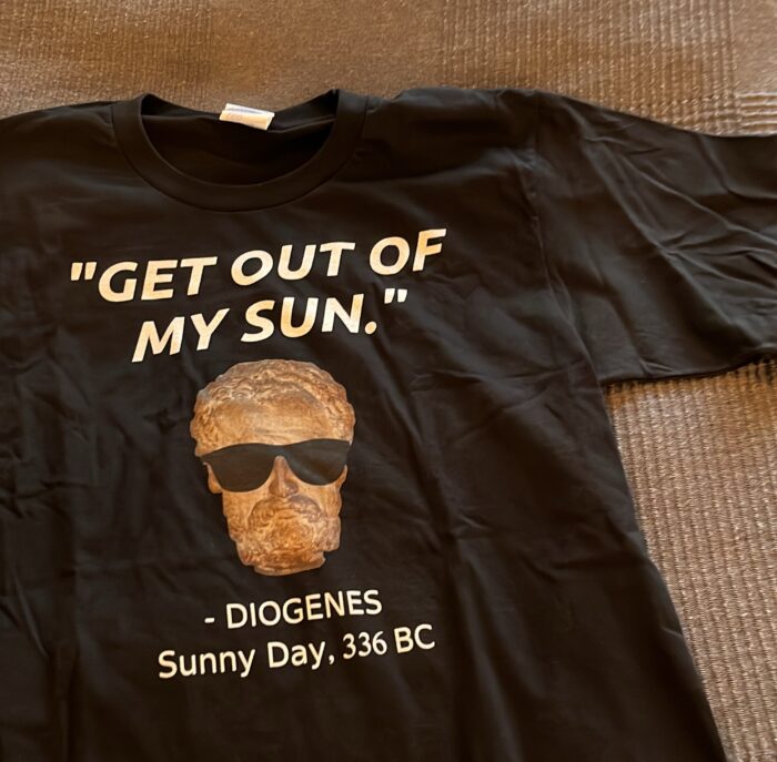 Ein schwarzes T-Shirt, darauf eine Diogenes-Büste mit Sonnenbrille und dem Satz "Get out of my sun"