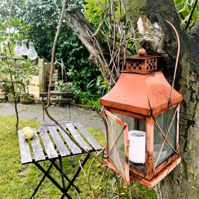 Fallobst auf einem Holztisch im Garten, im Vordergrund eine Laterne mit einer Kerze darin an einem Baum