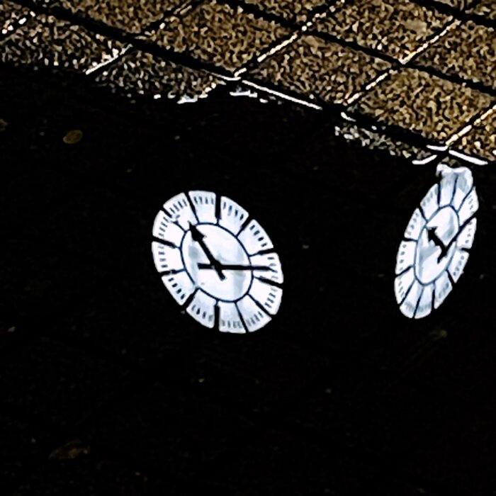 Uhren am Turm des Hauptbahnhofs spiegeln sich in einer abendlichen Pfütze auf dem Bahnhofsvorplatz. ein sehr dunkles Bild