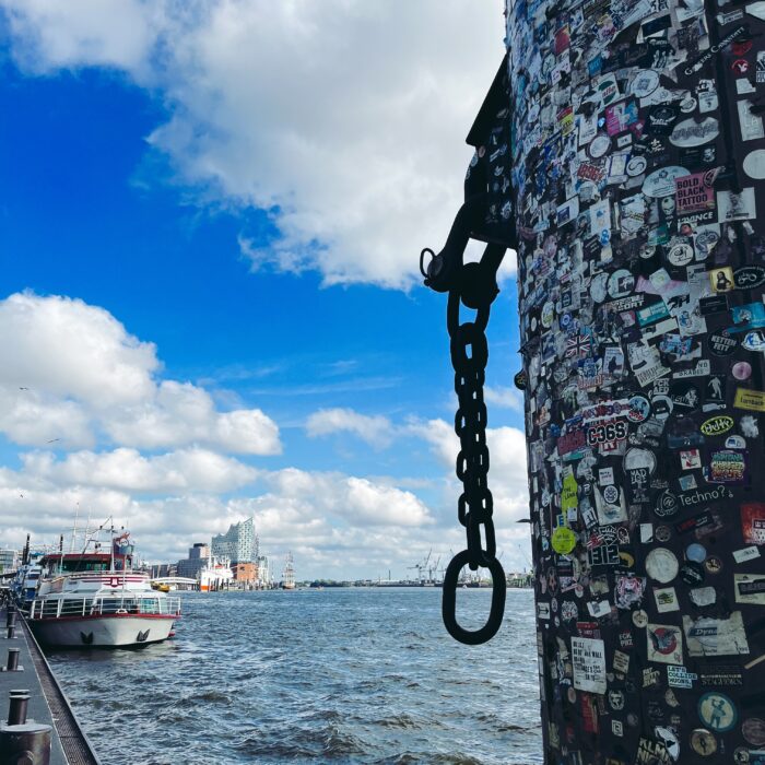 Blick von den Landungsbrücken Richtung Elbphilharmonie, im Vordergrund ein Poller, übersät mit Aufklebern
