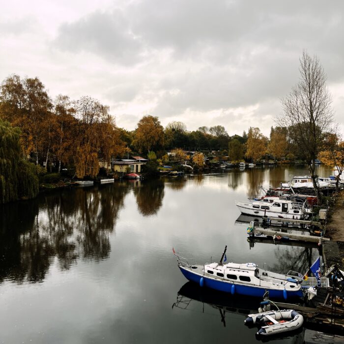 Blick über die Bille an der Billerhuder Insel, Boote an Stegen, grauer Himmel, Herbstlaub an den bäumen