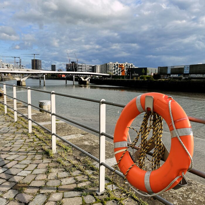 Blick auf die Neubebauung am Baakenhafen, im Vordergrund ein Rettungsring am Geländer des Weges neben dem Elbeseitenarm