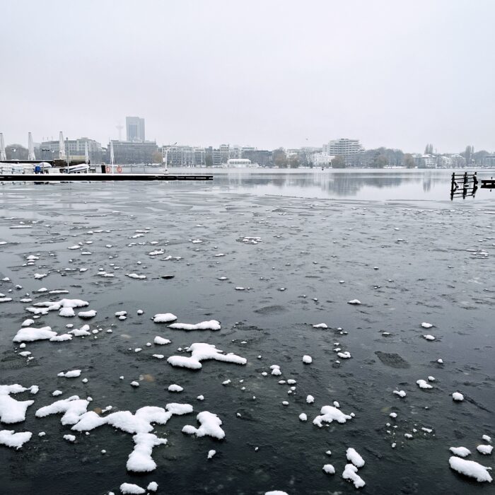 Blick über die dünn vereiste Außenalster vom Anleger am Hotel Atlantic aus, weiße Schneereste auf schwarzer Eisfläche