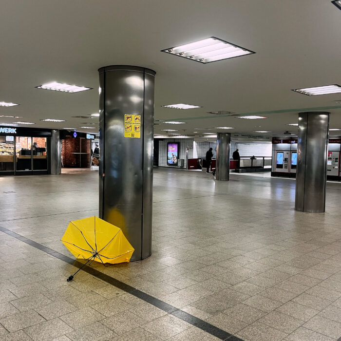 Ein ramponierter gelber Regenschirm liegt im U-Bahn-Bereich des Hauptbahnhofs und formt einen Halbkreis, wie wie aufgehende Sonne