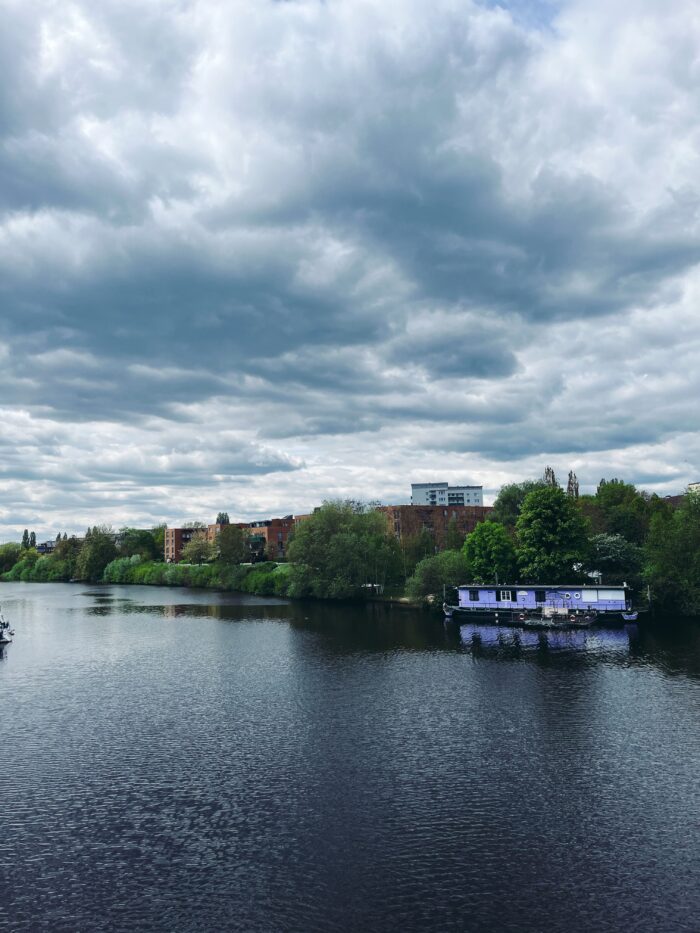 Bedrohlich wirkende Wolken über der Bille, ein lilafarbenes Hausboot am Ufer