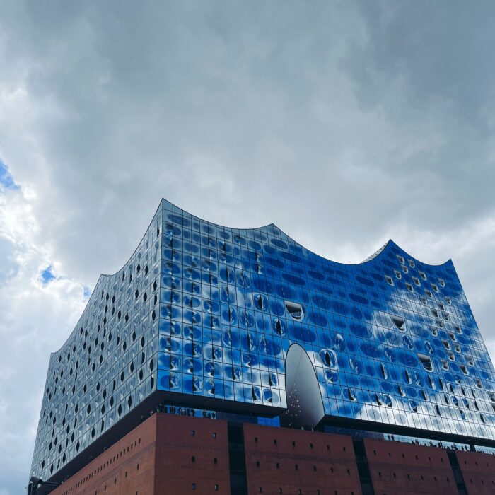 Die Elbphilharmonie in klassischer Touristenansicht, Wolken und blauer Himmel spiegeln sich in den zahllosen Scheiben