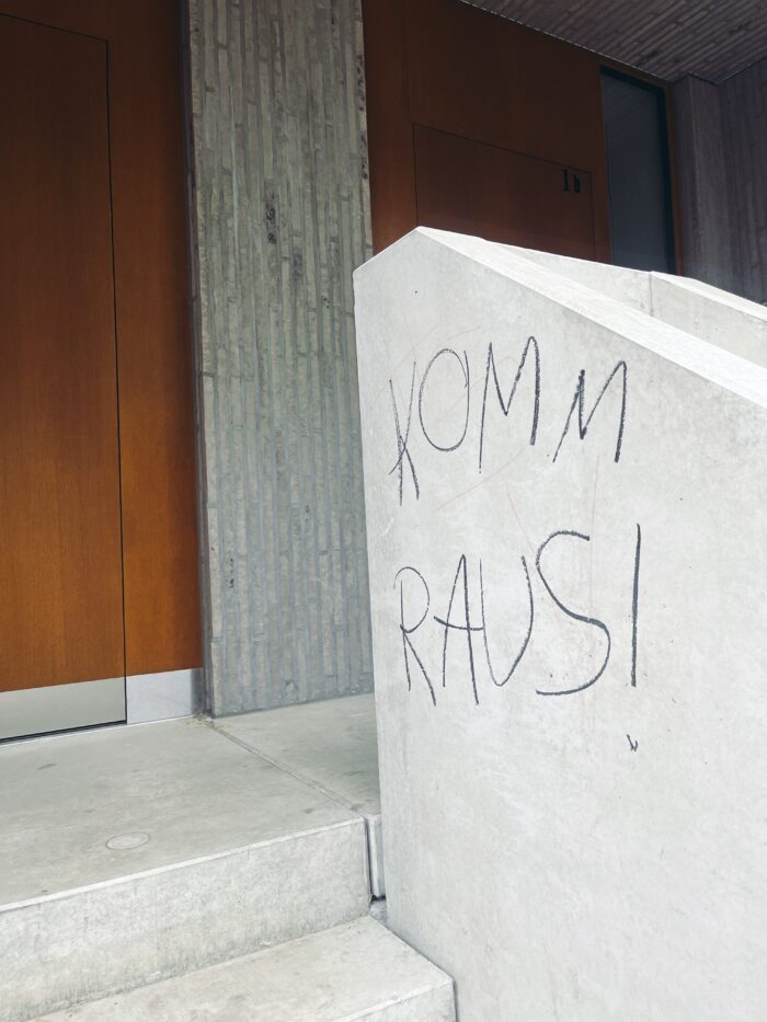 Der Schriftzug "Komm raus" auf einer Wand an einem Treppenaufgang vor einem Haus