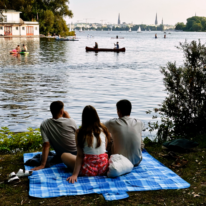Zwei Männer und eine Frau auf einer Picknickdecke am Ufer der Außenalster