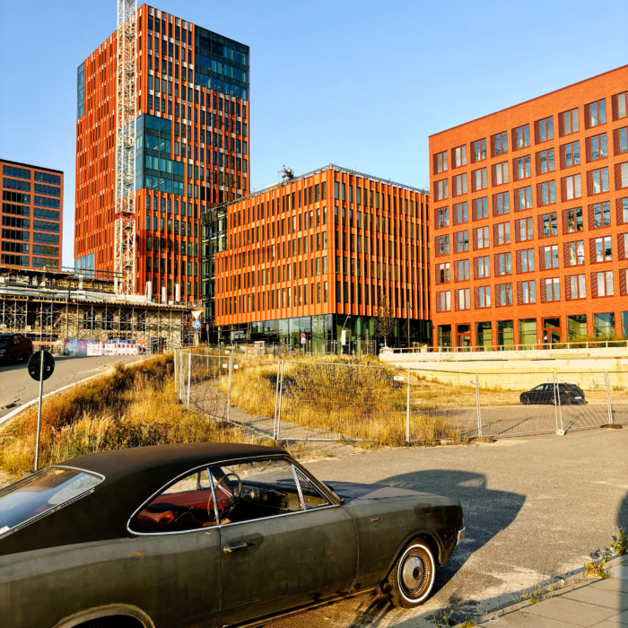 Ein altes Auto mit sportlicher Anmutung vor neuen Bürogebäuden im Elbbrückenquartier