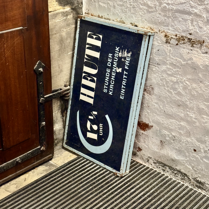 Ein altes Schild in einer Kirchenecke abgestellt, es weist auf die Stunde der Kirchenmusik in St. Petri hin