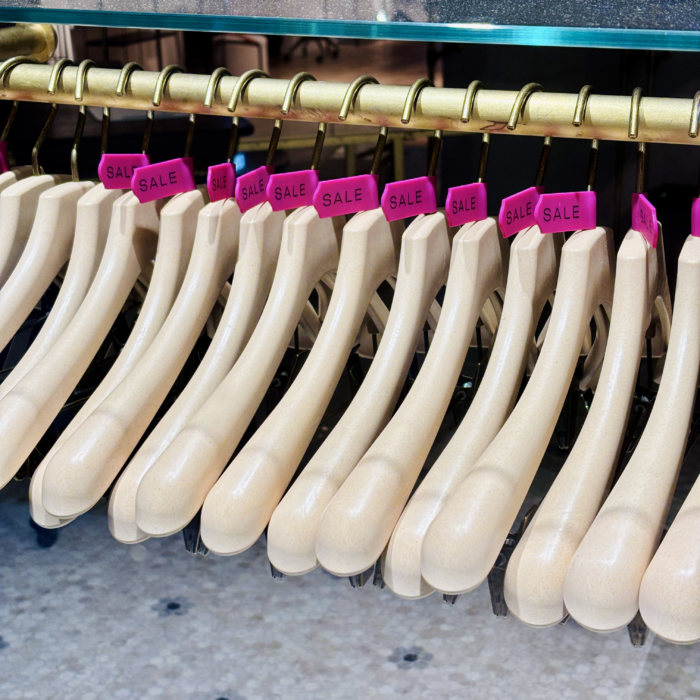 Leere Kleiderbügel in einem Schaufenster, jeder trägt einen lilafarbenen "Sale"-Plastik-Clip am Haken