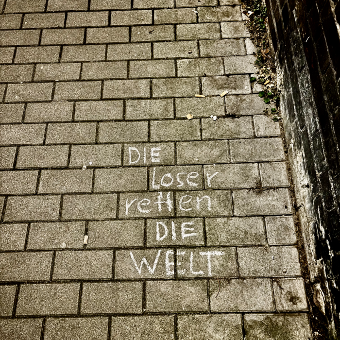 Kreideschrift auf dem Pflaster: Die Loser retten die Welt