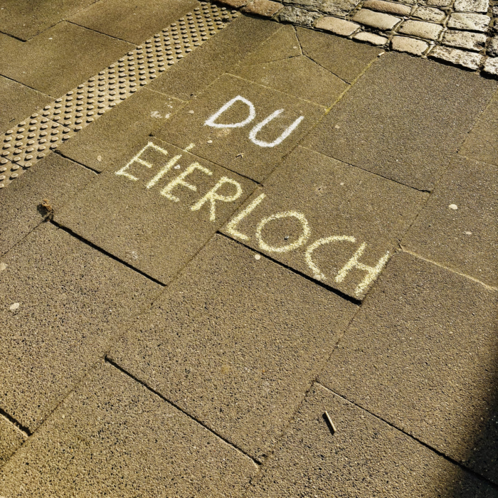 Kreideschrift auf einem Fußweg: "Du Eierloch"