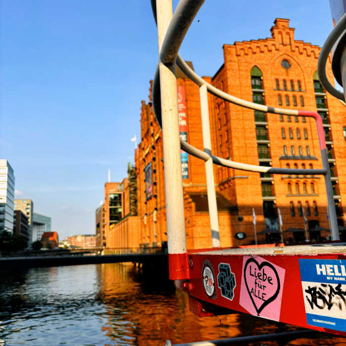 Hafencity, Blick über Wasser auf die Rückseite des Maritimen Museums, im Vordergrund ein Aufkleber an einem Metallgestänge: "Liebe für alle"