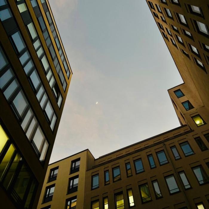 Blick aus einem Innenhof zwischen Neubauten nach oben, Abendlicht, oben eine Mondsichel
