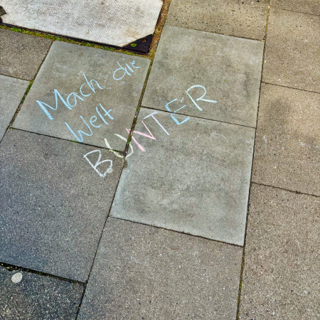 Farbiger Kreideschriftzug auf dem Pflaster: "Mach die Welt bunter"
