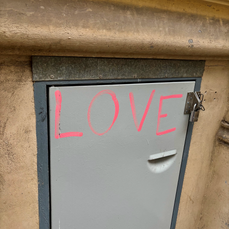 Der Schriftzug "Love" in pinkfarbener Schrift auf der Tür zu einem Verschlag für Container an einem Wohnhaus