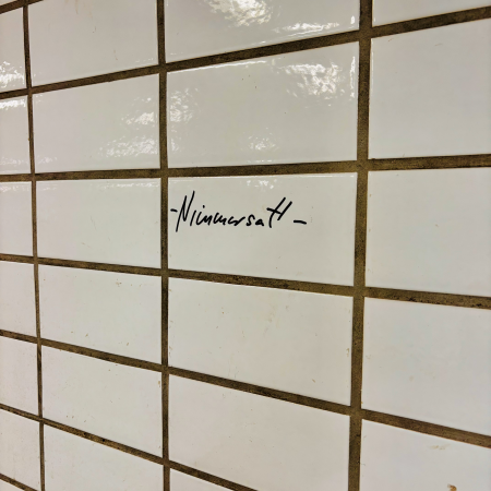 Das mit Edding geschriebene Wort Nimmersatt auf den weißen Kacheln einer U-Bahnstation