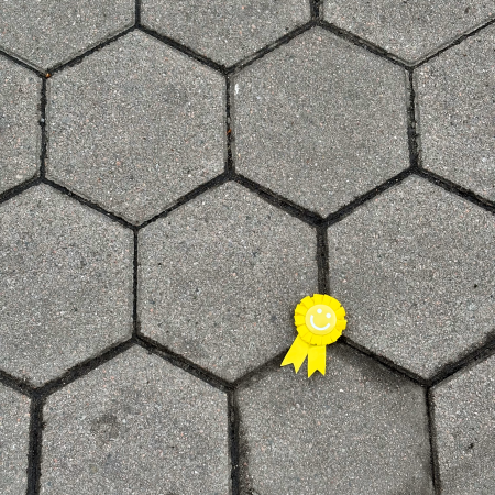 Eine Art Papierorden mit einem Smiley, der weggeworfen auf dem Pflaster liegt