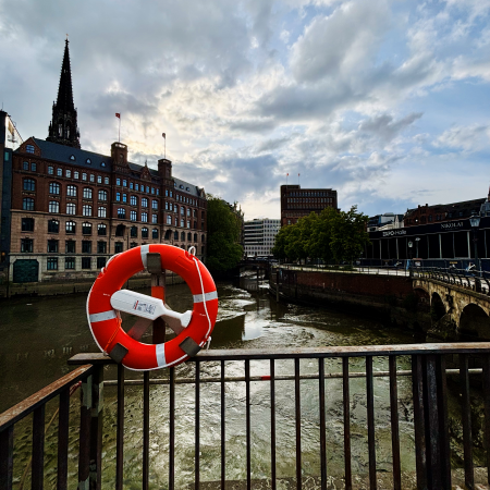 Ein Rettungsring an der Trostbrücke in der Innenstadt, dahinter der trockengefallene Fleet
