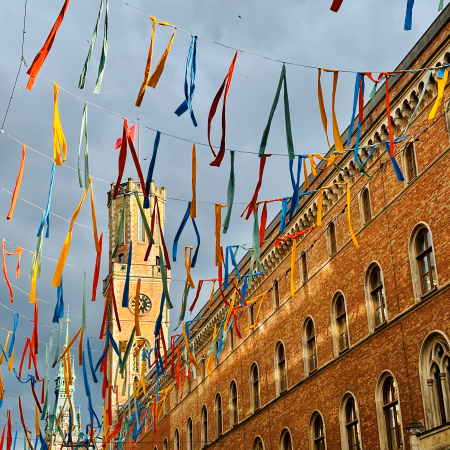 Poststraße, Blickm auf die alte Post mit flirrender, bunter, sommerlicher Deko über Straße, bunte Stoffstreifen im Wind