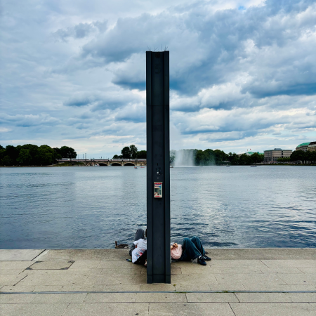 Menschen sitzen am Anleger Jungfernstieg, im Hintergrund die Binnenalster mit der Fontäne