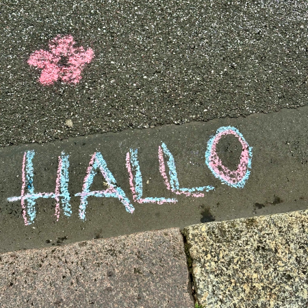 Kreideschrift auf dem Pflaster: "Hallo", daneben ein gemaltes Bümchen