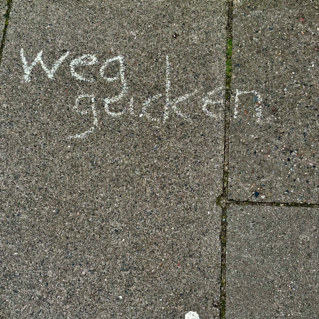 Kreideschrift auf dem Pflaster: "Weggucken"