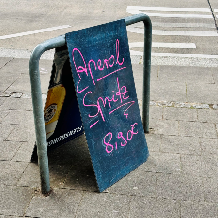 Ein Hinweisschild vor Außengastronomie, eine Tafel mit der Aufschrift "Aperol Spritz 8,90"