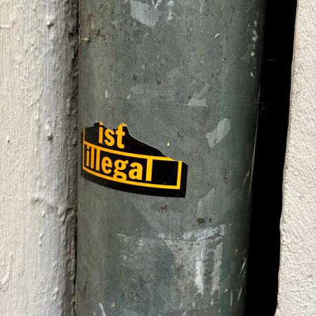 Ein abgerissener Aufkleber an einem Regenfallrohr, man kann nur noch "ist illegal" lesen