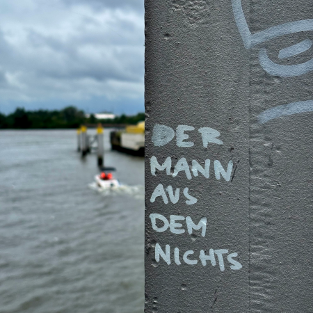 Schrift auf einem Brückenpfeiler in der Hafencity: "Der Mann aus dem Nichts". Im Hintergrund unscharf ein Motorboot