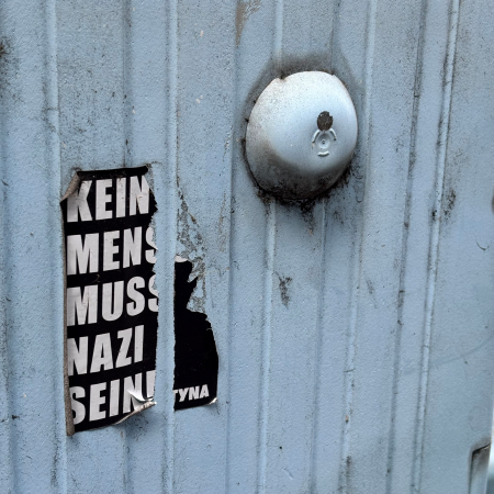 Ein beschädigter, aber noch lesbarer Aufkleber an einem Stromkasten: "Kein Mensch muss Nazi sein."