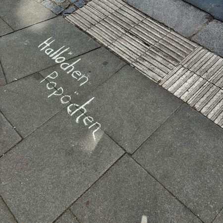 Kreideschrift auf dem Pflaster: Hallöchen Popöchen