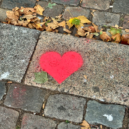 Ein auf das Pflaster gesprühtes Herz, daneben erstes Herbstlaub
