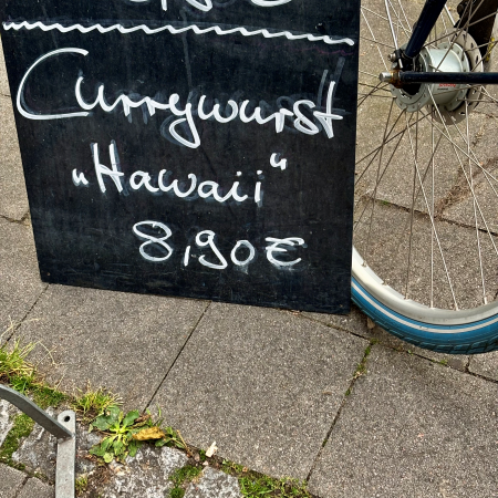 Eine Tafel vor einem Restaurant mit der Aufschrift "Currywurst Hawaii"