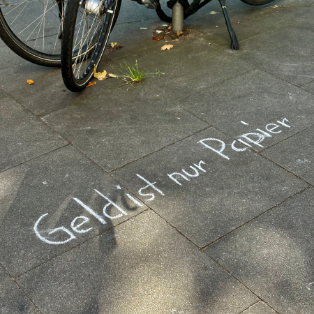 Kreideschrift auf dem Pflaster: Geld ist nur Papier