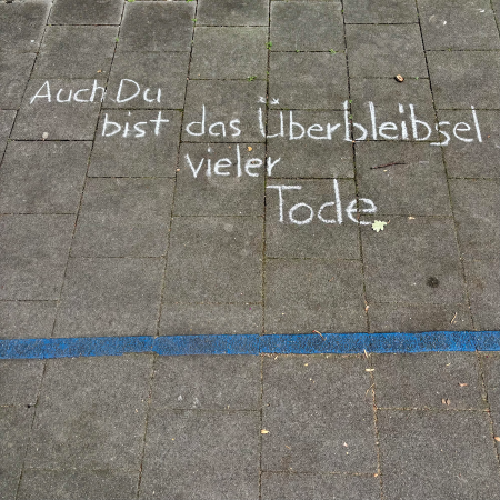 Kreideschrift auf dem Pflaster: "Auch du bist das Überbleibsel vieler Tode"